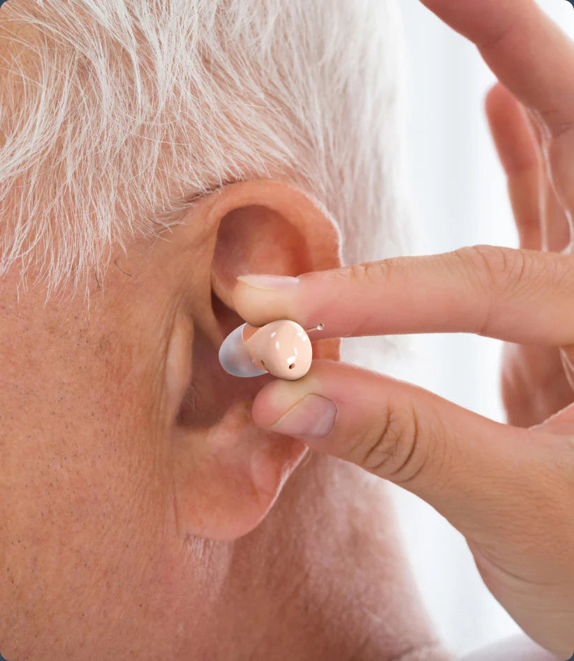 Person fitting a hearing aid into an elderly person's ear.
