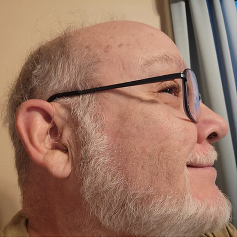 Close-up profile of older man wearing Audien in-ear hearing aid, smiling with satisfaction